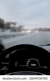 Windshield full of raindrops while driving on a road rainy weather at dusk driver's point of view