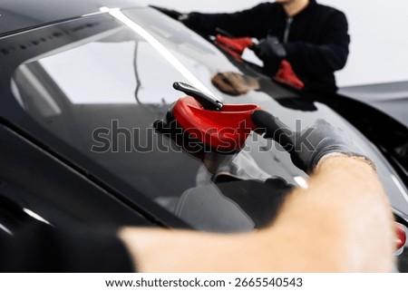 Windshield Installation Using Suction Lifters. Two technicians install windshield using suction lifters. Windshield placement ensures secure seal and integrity. New Windshield installation process