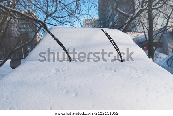 The windshield wipers\
of the car stick out of the snow. Thick layer of snow on the car.\
Car windshield under snow. Heavy snowfall, wintertime. Bad weather\
conditions.