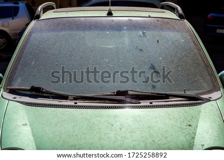 windshield with wipers dirty car in a layer of dry dirt and dust, closeup on a car theme.