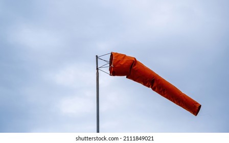 Windsock blowing on cloudy sky. Red cone, wind speed and direction indicator. Windy day at the airport. 