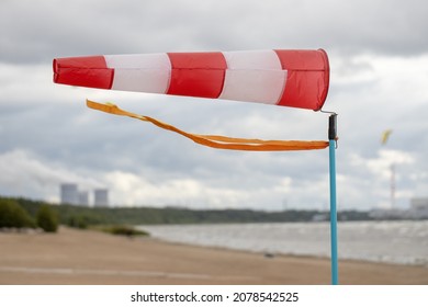 Windsock on a sandy beach in strong wind, Red and white fabric cone designed to indicate the direction and approximate wind speed, coastline, stormy sea with waves