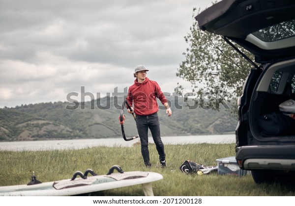 Windsurfer and camper packing and unpacking from
a car in nature.