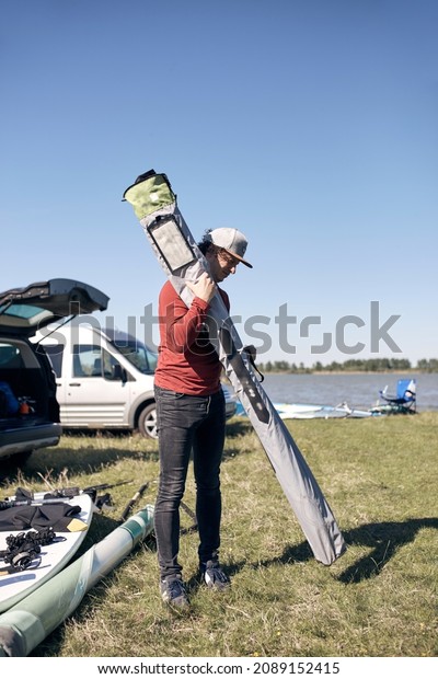 Windsurfer and camper packing and unpacking from\
a car in nature.