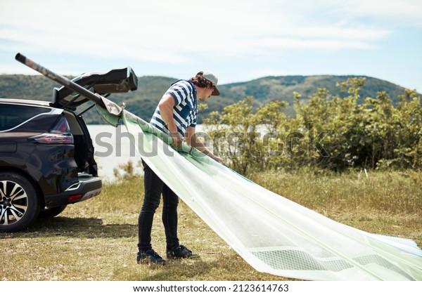 Windsurfer and camper packing and unpacking from\
a car in nature.