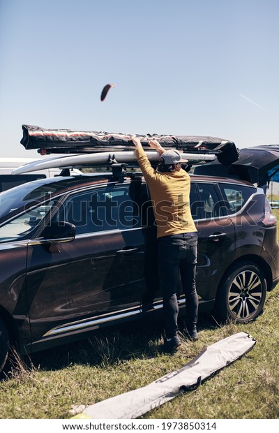 Windsurfer and camper packing and unpacking from
a car's roof rack in
nature.