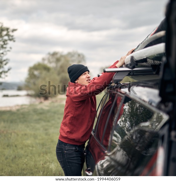 Windsurfer and camper packing and unpacking from\
a car\'s roof rack in\
nature.