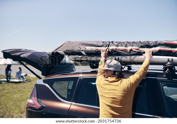 Windsurfer and camper packing and unpacking from\
a car\'s roof rack in\
nature.
