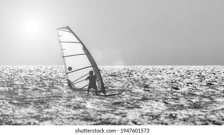 Windsurfer silhouette against a sunset background. Windsurfer Surfing The Wind On Waves, Recreational Water Sports, Extreme Sport Action. Sporting Activity. Healthy Active Lifestyle. Summer Fun.