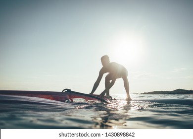 Windsurfer stands up on the board. Silhouette of surfer balancing on windsurf board on sunset sea, copy space