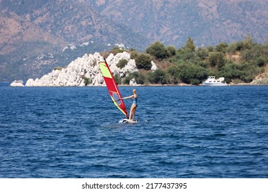 Windsurfing in the sea, water sports. View to woman windsurfer and green mountains in mist, scenic seascape - Powered by Shutterstock