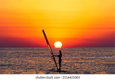 Windsurfing at sunset horizon view. Windsirfer girl at sunset. Sunset windsurfing. Windsurfing at sunset