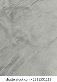 Wind-Swept Sand Patterns on the Beach. A vertical close-up highlighting subtle waves and flowing wind-swept patterns formed naturally on the surface of fine beach sand.