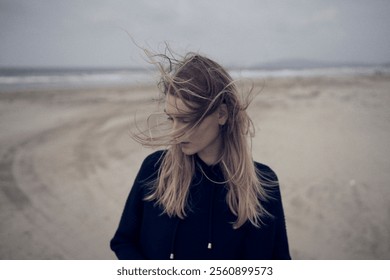 Wind-Swept Woman in a Hoodie Standing on a Moody Beachfront, Capturing Serenity and Isolation.