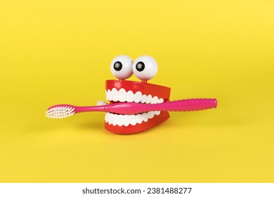 Wind-up toy mouth and nose with a toothbrush on a yellow background. The concept of oral care.