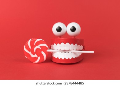 A wind-up toy with teeth and eyes with a lollipop on a red background. The concept of a holiday and parties. - Powered by Shutterstock