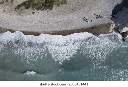 Windy waves crashing on a pebble beach. Drone aerial of stormy sea. Group of people at the beach. - Powered by Shutterstock