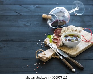 Wine appetizer set. Glass of red wine, French sausage and olives on black wooden backdrop, selective focus