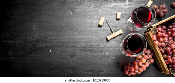 Wine background. Red wine in an old box with a corkscrew. On the black chalkboard.
