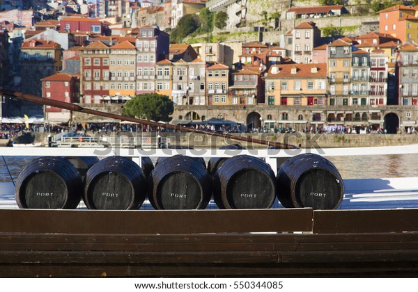 Wine barrels in Porto. Five\
barrels of Port wine on a boat. The town of Porto as a background.\
