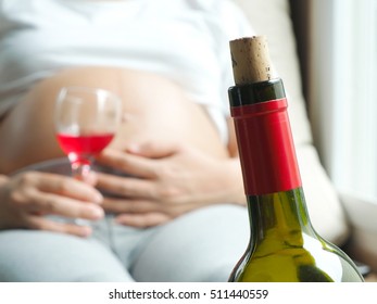 Wine bottle with background of pregnant woman with glass of wine in hand. Concept of pregnancy health care.