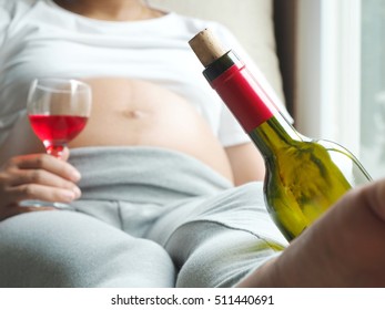 Wine bottle with background of pregnant woman with glass of wine in hand. Concept of pregnancy health care.