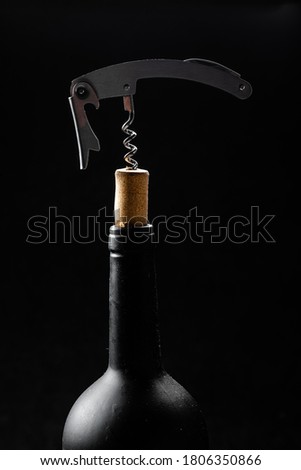 Wine bottle being opened with corkscrew on table on black background. Step-by-step instructions on how to use the corkscrew to open a bottle of wine.