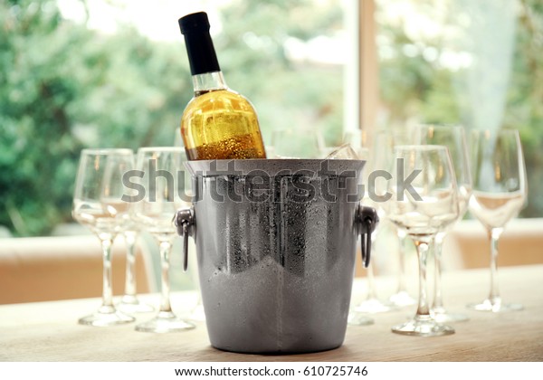 Wine\
bottle in bucket with ice and glasses on\
table