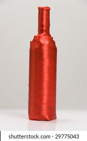 A Wine Bottle Gift Wrapped In Red Ribbon Against A White Background