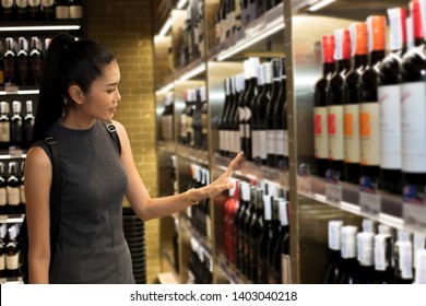 Wine Cellar Shop With Many Bottles Brand On Shelf And Pick Up Select By Asian Black Hair Adult Working Woman, In Temperature Control Room To Keep Winecellar Fresh Long Time, Concept Decision Making