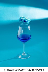 Wine Glass With Blue Liquid And Spring  Flower Above It. Strange Lights And Shadows Making Scene. Blue Performance Aesthetic Design Idea