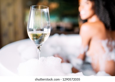 Wine Glass With Blurred Happy Black Young Woman Relaxing In The Hydro Massage Bath