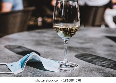 Wine Glass And Face Mask On A Table. Measures In Outdoor Cafe, Bar Or Restaurant After Reopening After Quarantine.