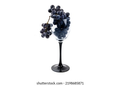 A wine glass filled with a bunch of blue concord grapes isolated on white