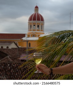 wine glass held by the hand of a man with the Cathedral Church Inmaculada Concepción de María, Granada (Nicaragua) in the background