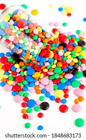 A Wine Glass Remains Tipped Over A Table With Multicolored Chocolate Dragees Going Out From It. Studio Photo Isolated On White. Selective Focus.