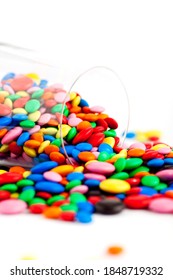 A Wine Glass Remains Tipped Over A Table With Multicolored Chocolate Dragees Going Out From It. Studio Photo Isolated On White. Selective Focus.