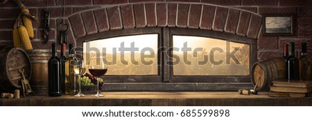 Wine glasses, bottles and barrels in a rustic countryside wine cellar; panoramic window view of lush vineyards at sunset: traditional winemaking concept