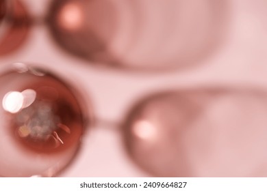 Wine glasses defocused, rose wine blurred on pink background with light flare, optical blur, bokeh. Top view aesthetic still life monochrome photo alcohol drink for winery, wine list, copy space.