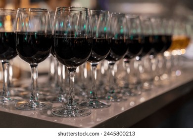 Wine glasses filled with red wine arranged and presented on a table top for self-service by party guests. Shallow depth-of-field image. A glass of red wine is on the table. Glasses of wine. 