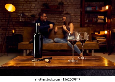 Wine Glasses Of Red Wine On Table At Home Happy Love Couple Talking In Background. 