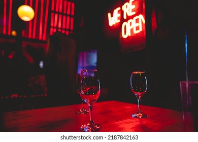 Wine glasses and 'we're open' red neon sign in the night