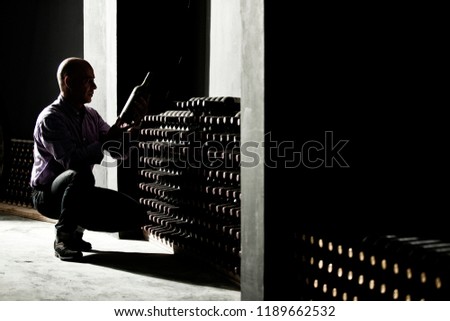 Wine maker checking horizontal bottles in a dark cellar