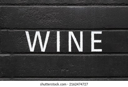Wine painted on black wall. White capital letters on black surface. Alcoholic beverage or drink advertisement backdrop. Pub, bar, restaurant or wine store background texture or signage. 