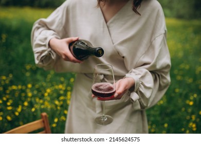 Wine pouring from bottle, outdoor picnic. Pouring red wine into a glass in the garden. 