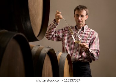 Wine Producer In Cellar Taking Sample Of White Wine From Barrel For Wine Tasting.
