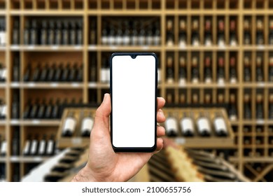 Wine Shop With Bottles Background. Hand With Blank Smartphone Screen One Wine Backdrop. Buying And Ordering Alcoholic Beverages Online