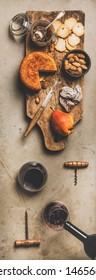 Wine and snack set. Flat-lay of two glasses of red wine, vintage corkscrews, cheese and appetizers on board over concrete background, top view, vertical composition. Party food concept