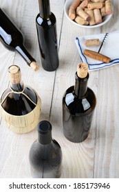 Wine still life shot from a high angle. Five bottles of wine with a cork screw napkin and bowl of corks on a rustic farmhouse style table. Vertical format.