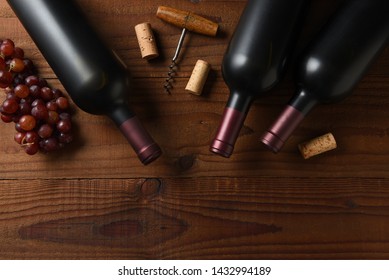 Wine Still Life: Three Cabernet Sauvignon Wine Bottle Short From Directly Above On A Dark Wood Table With Grapes Corks And Cork Screw And Copy Space.